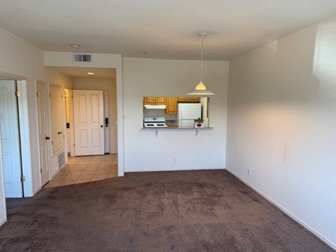 A room with a carpeted floor and a small kitchenette.