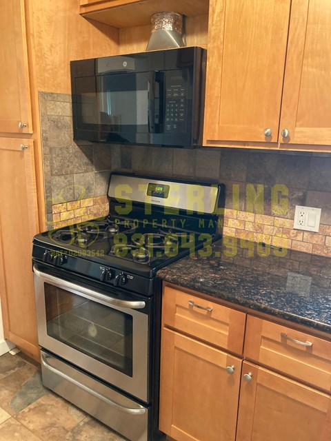 A black stove top oven with a silver oven door sits on a granite countertop.