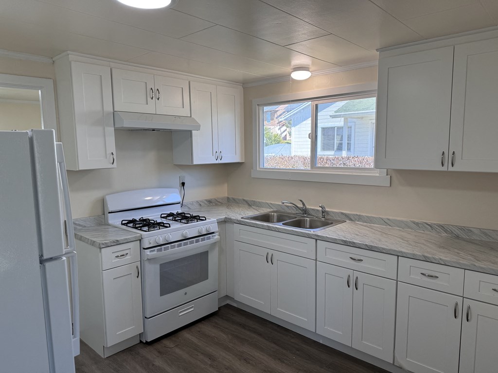 an empty kitchen with white cabinets and a stove and sink
