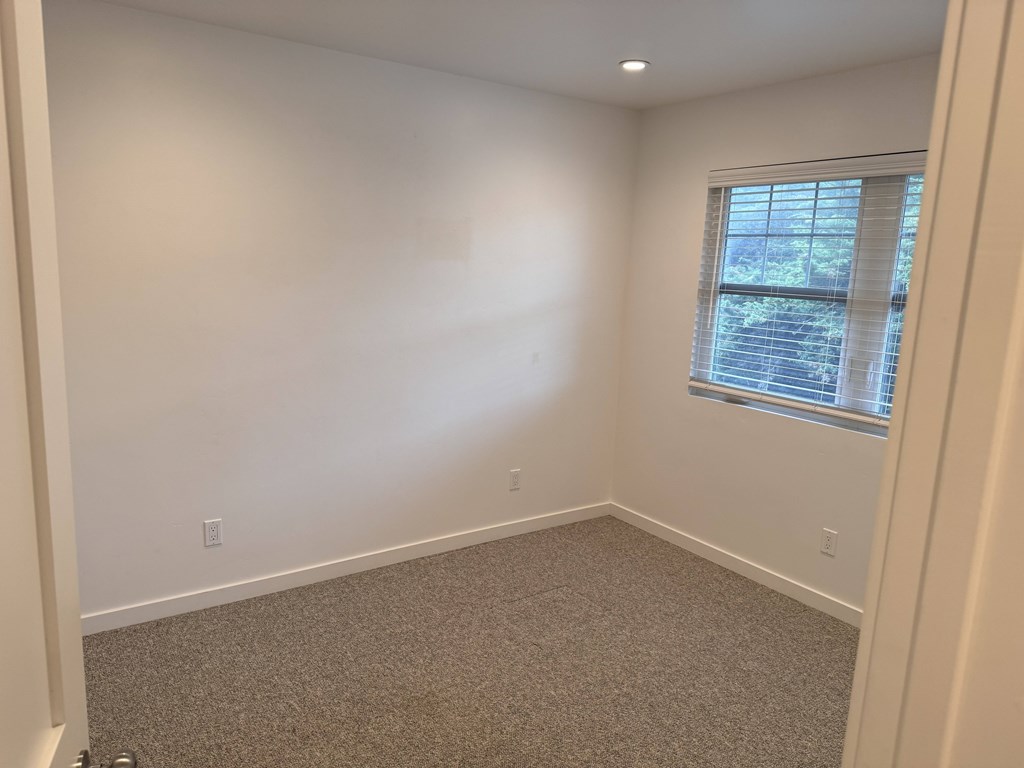 A room with a carpeted floor and a window with blinds.