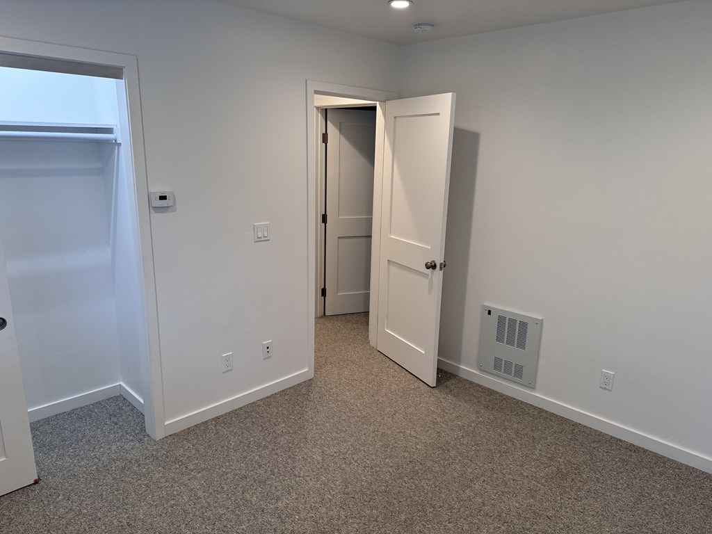 A room with a carpeted floor, a white door, and a white wall.