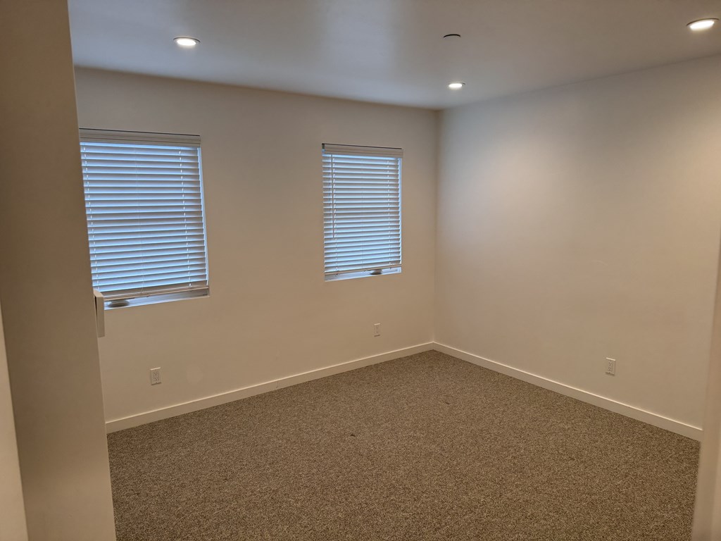 A room with carpeted floor and two windows with blinds.