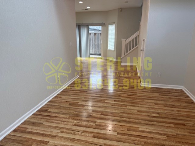 A room with wooden flooring and a staircase in the background.