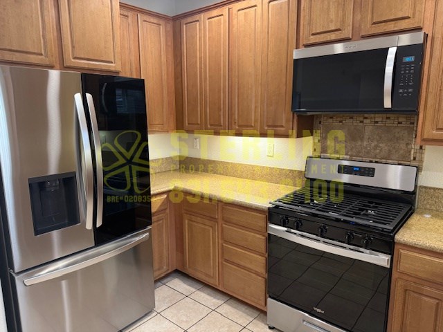 A kitchen with a stainless steel refrigerator, black microwave, and black stove top oven.