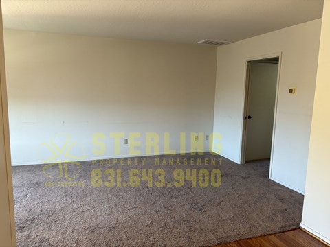 A room with a carpeted floor and a door, with a phone number for Sterling Property Management displayed on the wall.