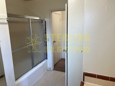 A bathroom with a glass shower door and a tiled floor.