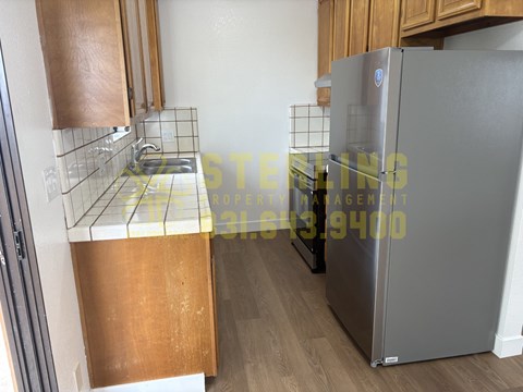 A kitchen with a refrigerator, sink, and wooden cabinets.