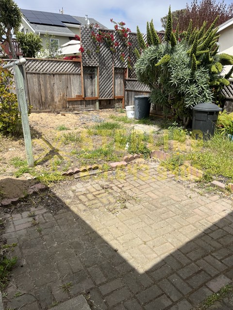 A backyard with a brick patio and a wooden fence.