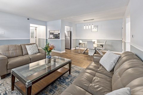 A living room with a glass coffee table and a brown leather couch.