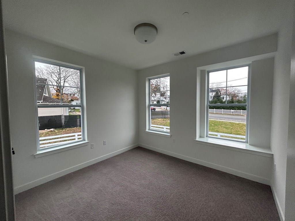 an empty living room with three windows and a carpet