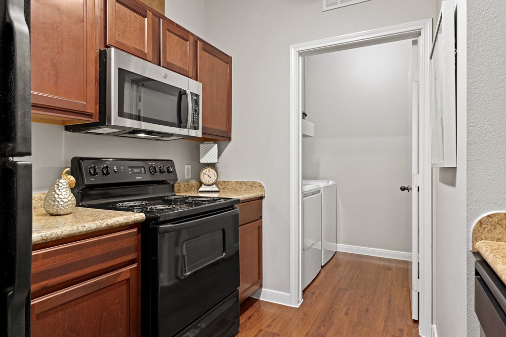 a kitchen with black appliances and wooden cabinets and a white door at Bella Madera Apartments, Lewisville, 75056