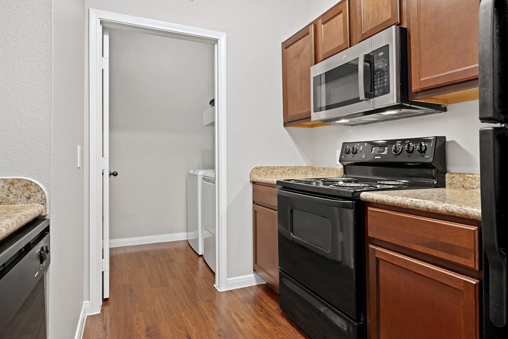 a kitchen with hardwood floors with brown cabinets at Bella Madera Apartments, Lewisville