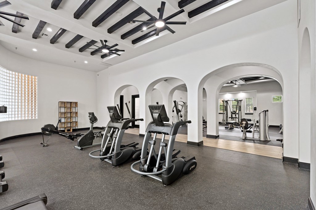 a gym with cardio machines and weights in a room with archways at Bella Madera Apartments, Lewisville Texas