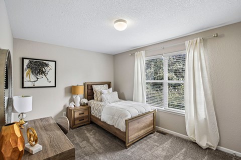 A bedroom with a large bed and a window with white curtains.