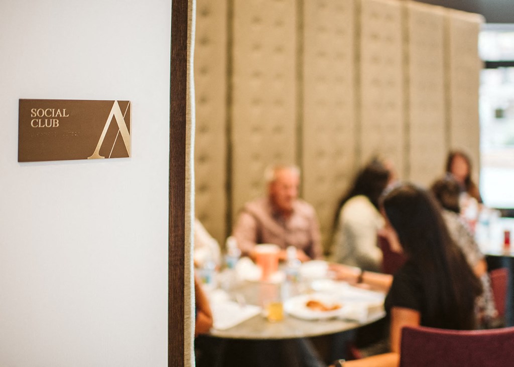 a plaque outside a conference room labeled social club with people sitting around tables in the background at The Apex at CityPlace, Kansas, 66210