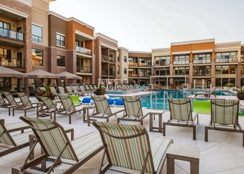Rows of chaise lounge chairs around an outdoor pool surrounded by apartment buildings - Photo Gallery 5