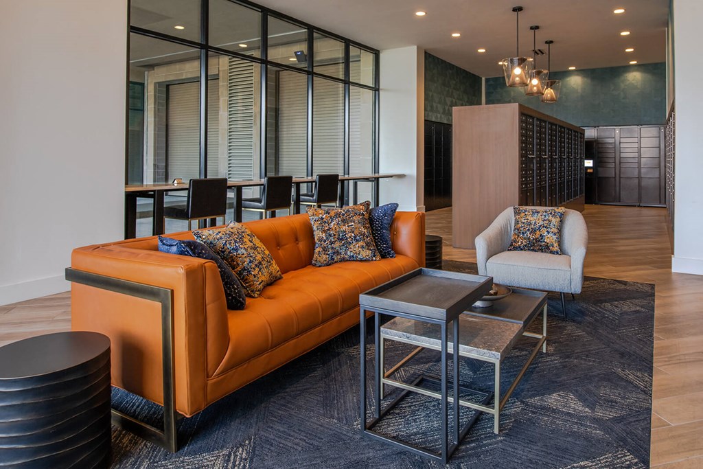 seating area with orange couch, white chair, and various sizes of side tables on a gray rug at The Apex at CityPlace, Overland Park