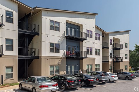 A row of apartment buildings with cars parked in front.