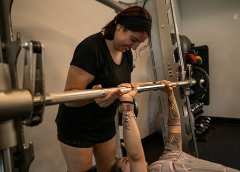 A woman is helping a man lift a barbell in a gym.