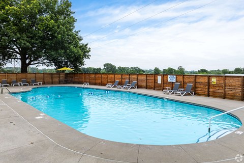 A rectangular pool with a concrete edge and a few chairs around it.