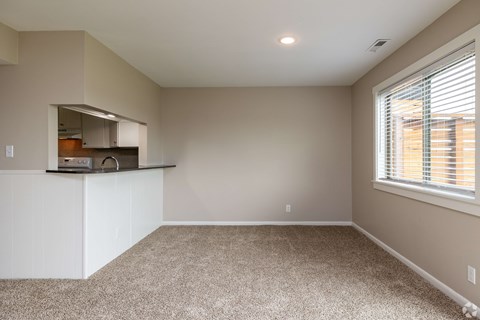 A spacious room with a window and a kitchen area in the background.