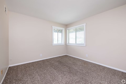 A room with carpeted floor and two windows.