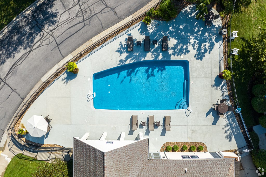 An aerial view of a swimming pool surrounded by a concrete patio and a building.