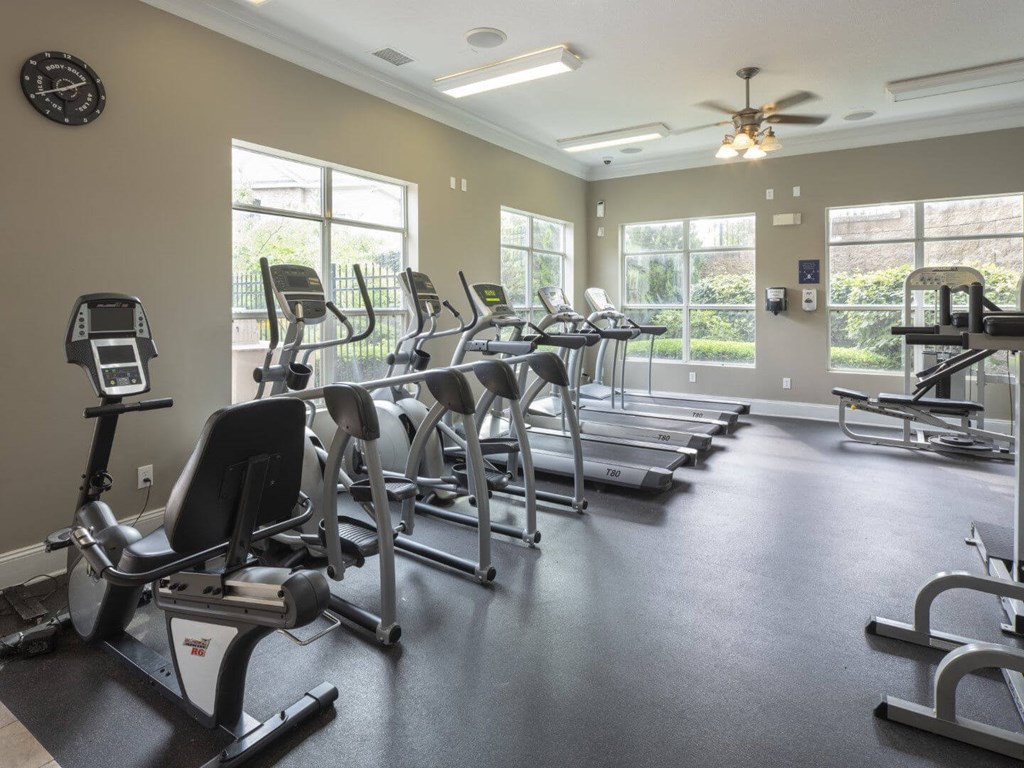 A spacious gym with treadmills, elliptical machines, and a ceiling fan.