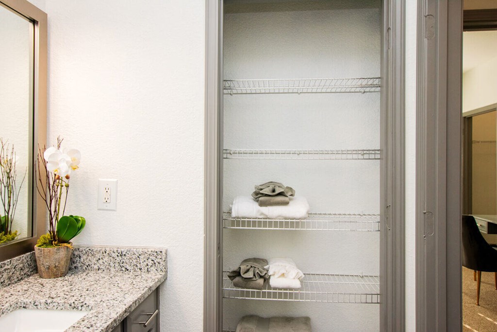 A bathroom with a large mirror, a sink, and a shelf with towels and toiletries.