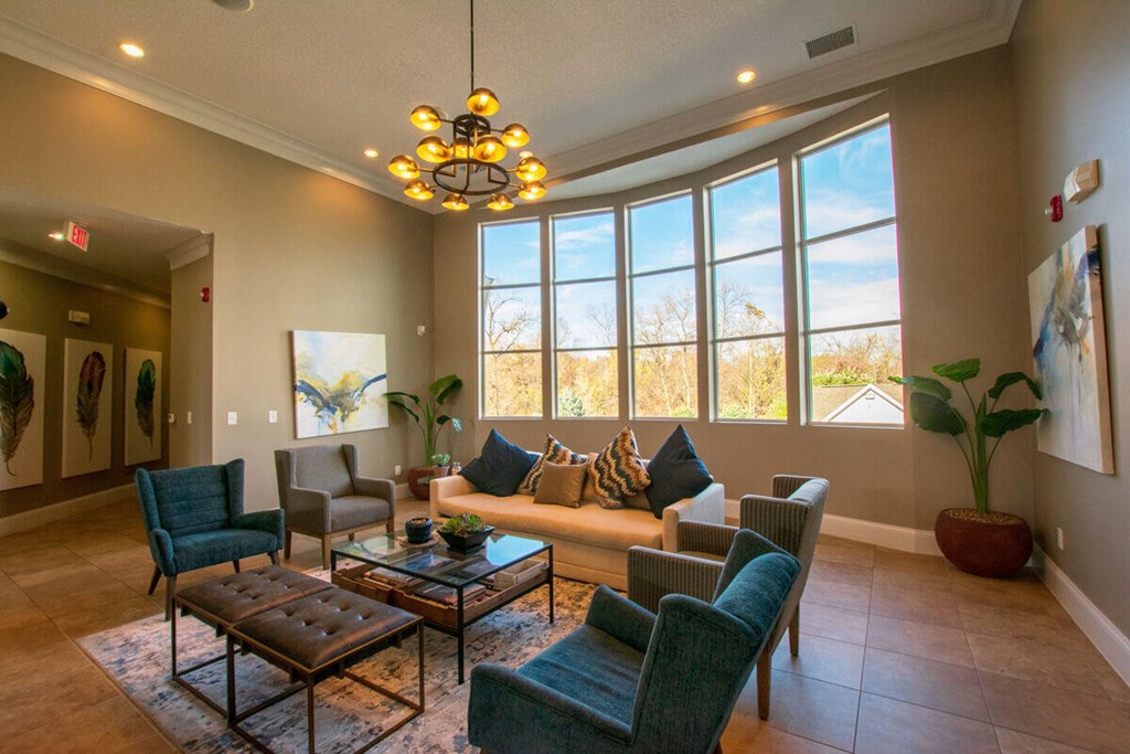 A living room with a brown leather ottoman and a glass coffee table with a chandelier hanging from the ceiling.