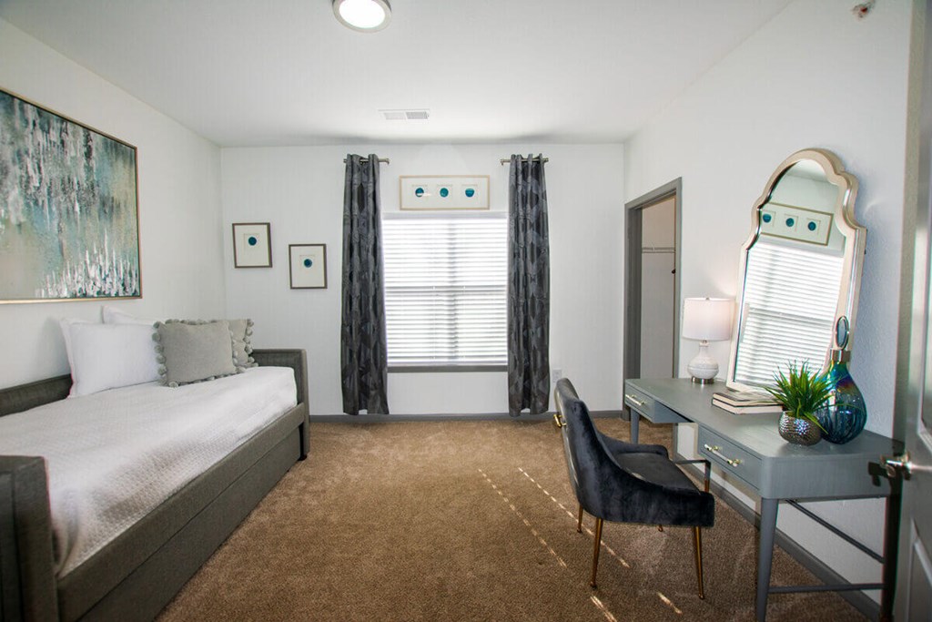 A bedroom with a bed, desk, chair, and a painting on the wall.