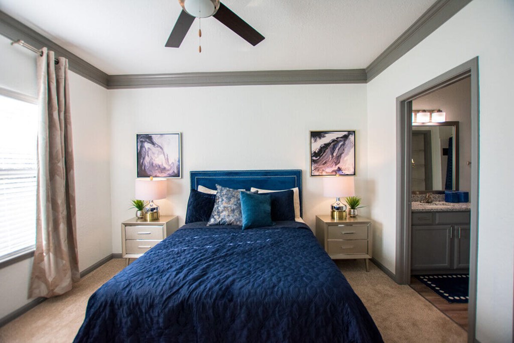 A bedroom with a blue bedspread and a ceiling fan.