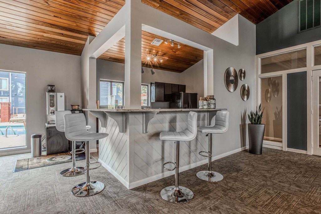 A modern bar area with white chairs and a wooden ceiling.