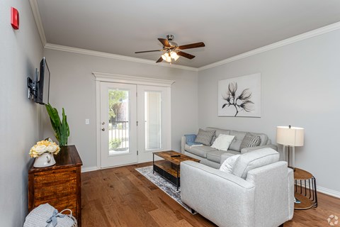 A living room with a grey couch, a wooden dresser, a ceiling fan, and a painting on the wall.
