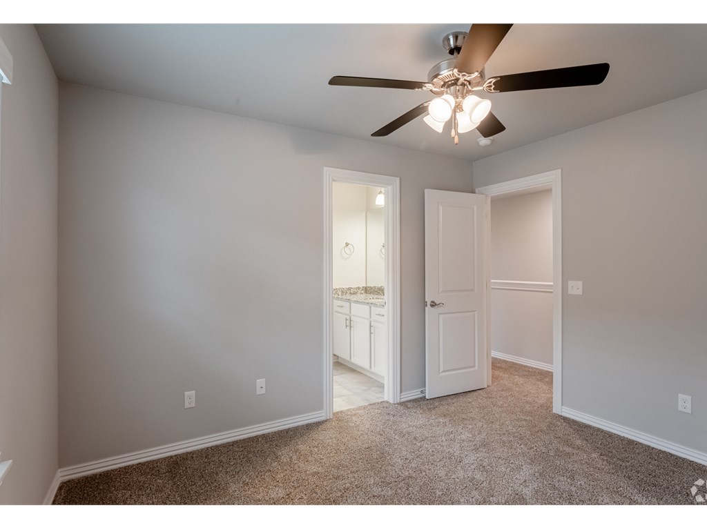 a bedroom with a ceiling fan and a door to a bathroom