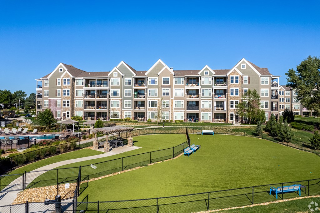 an exterior view of an apartment building with a green field and a tennis court  at Waterside Residences on Quivira, Lenexa, Kansas