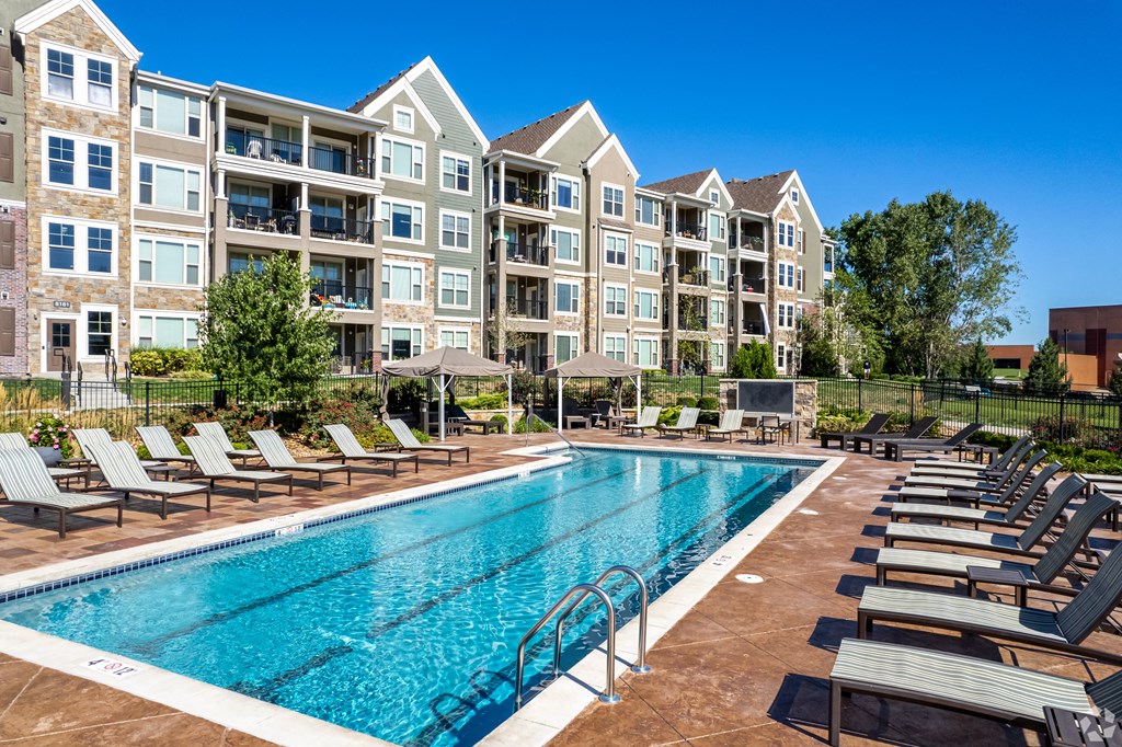 a swimming pool with lounge chairs in front of an apartment building  at Waterside Residences on Quivira, Lenexa, Kansas