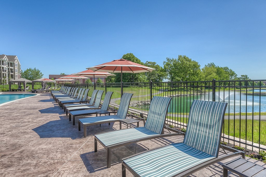 a row of lounge chairs and umbrellas next to a swimming pool  at Waterside Residences on Quivira, Lenexa, KS