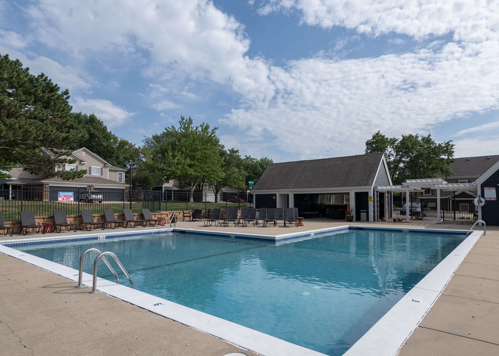 a swimming pool with chairs around it in front of a building a swimm at Centennial Park Apartments, Overland Park, Kansas