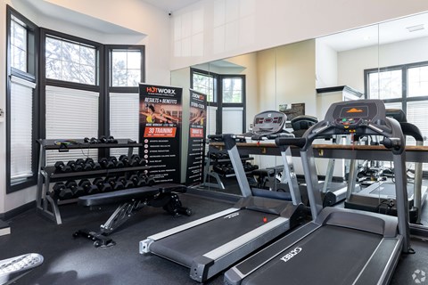 A gym with treadmills, dumbbells, and a sign that says "HIT WORKOUT RESULTS & REVIEWS".
