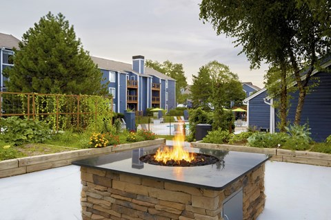 A fire pit in the middle of a garden with a building in the background.