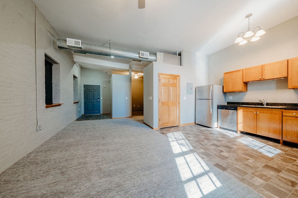 an empty living room and kitchen with wood cabinets and a refrigerator