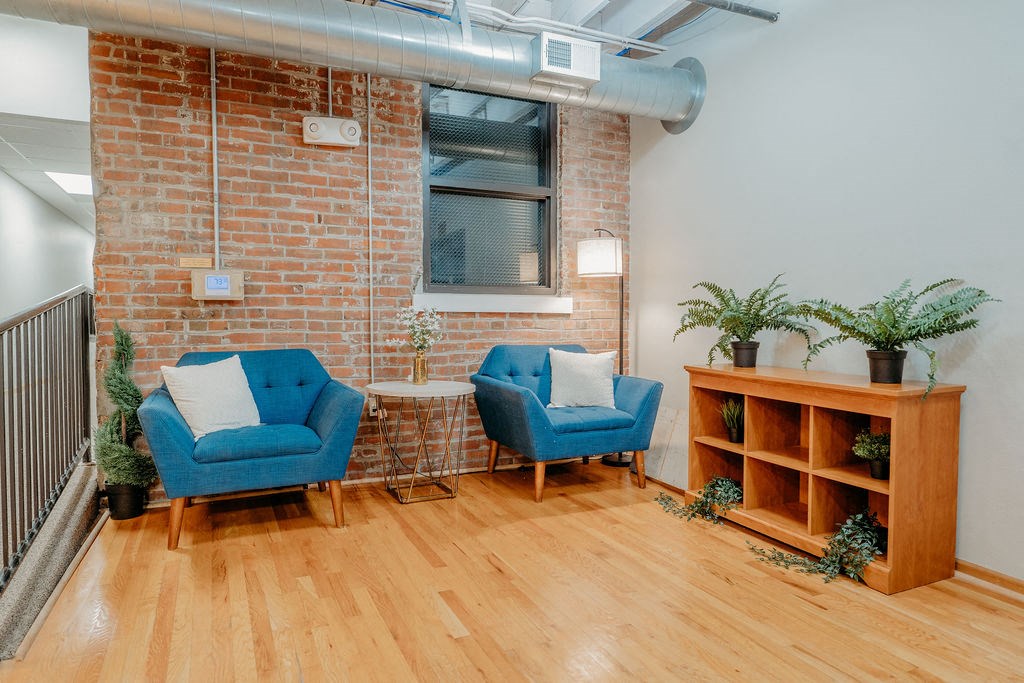 a living room with two blue chairs and a brick wall