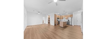 A spacious room with wooden flooring and a kitchen area in the background.