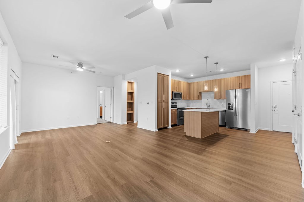 A spacious room with wooden flooring and a kitchen area in the background.