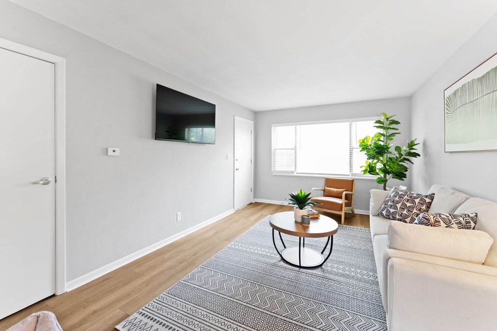 A living room with a white couch, a coffee table, and a flat-screen TV mounted on the wall.