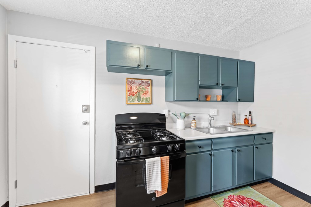 A kitchen with a black stove top oven and teal cabinets.