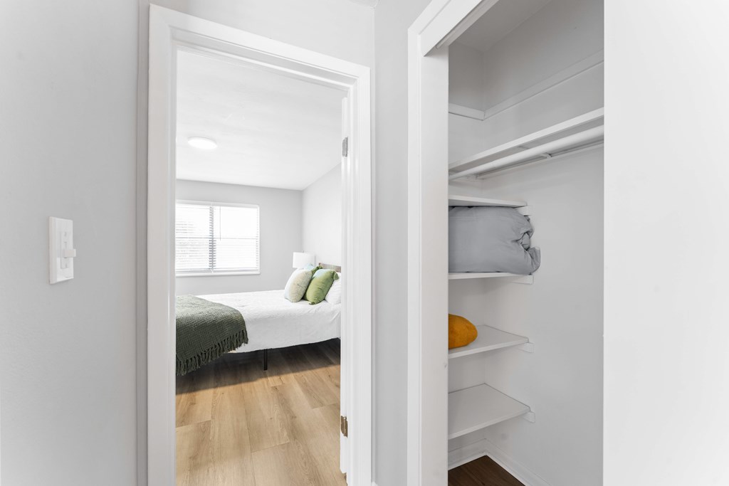 A white bedroom with a bed and a small closet.