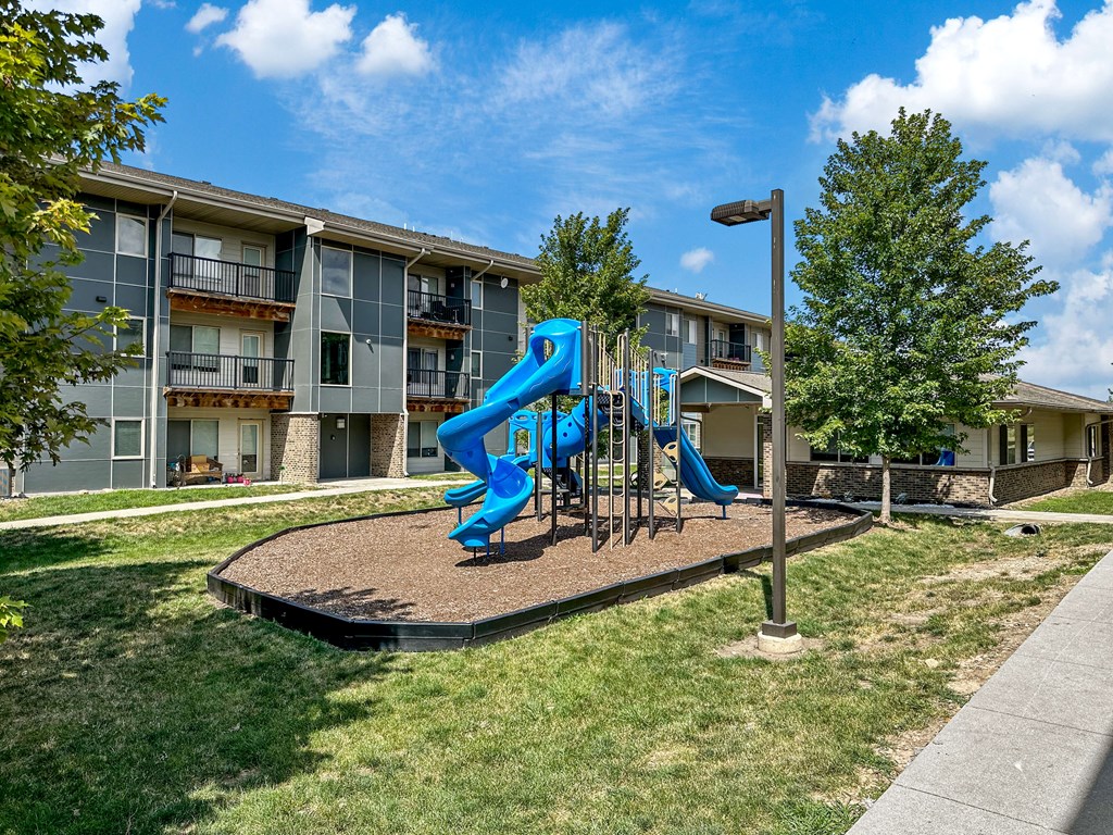 A playground with a blue slide in front of apartment buildings.