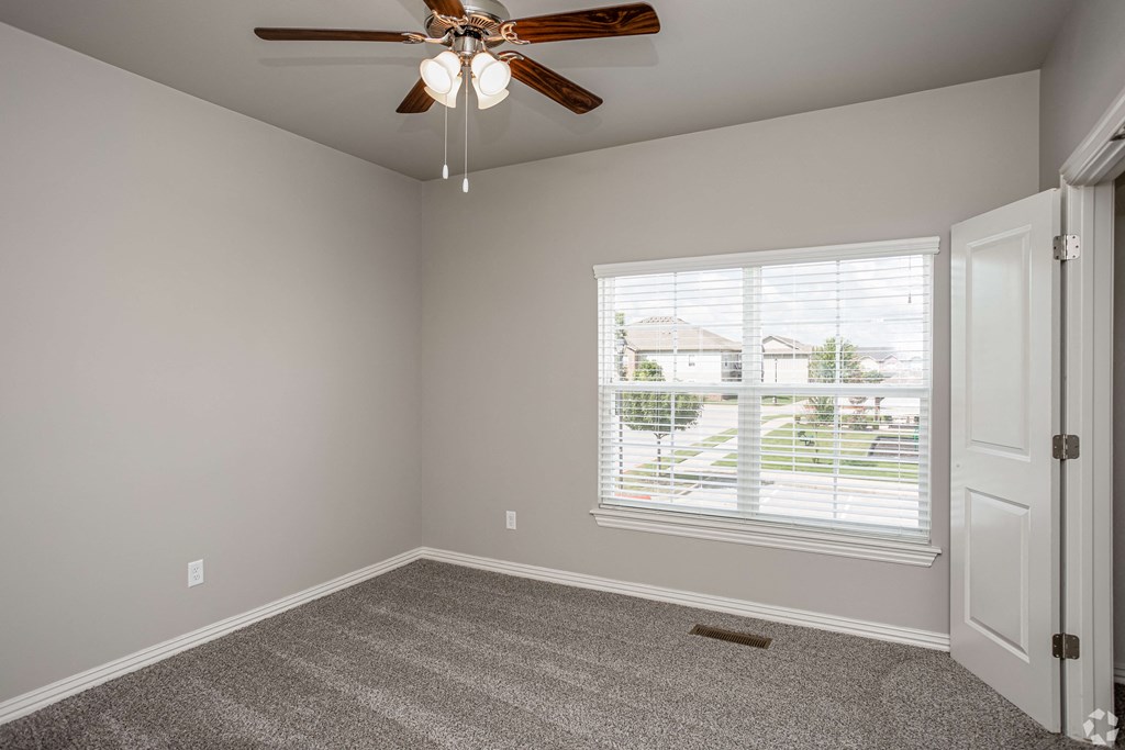 an empty bedroom with a ceiling fan and a window
